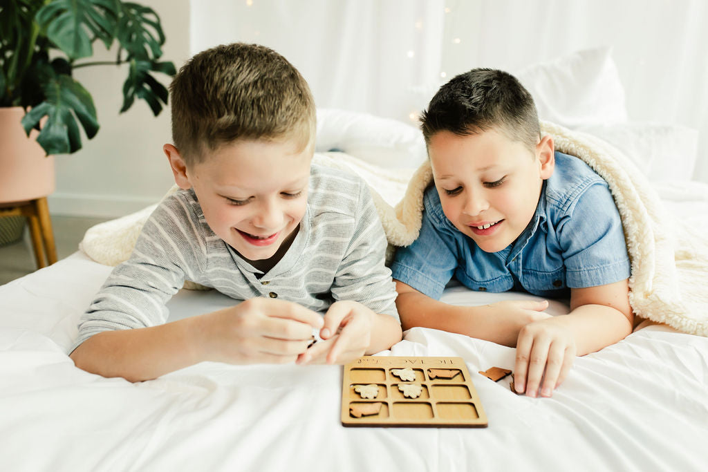 two boys laying on a bed playing with a wooden puzzle