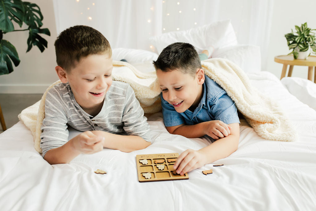 two boys laying on a bed playing with a board game